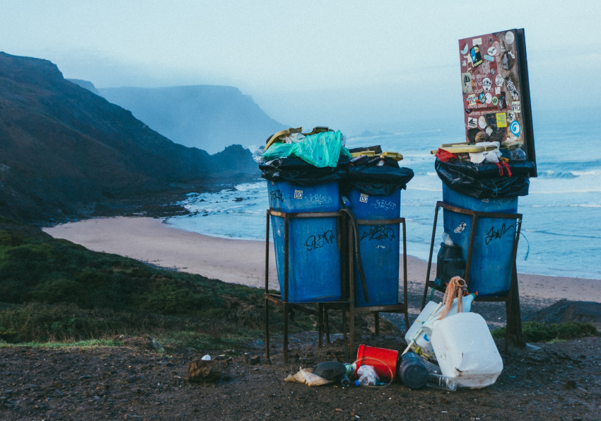 3 blue over-filled garbage cans in front of a ocean's seaside